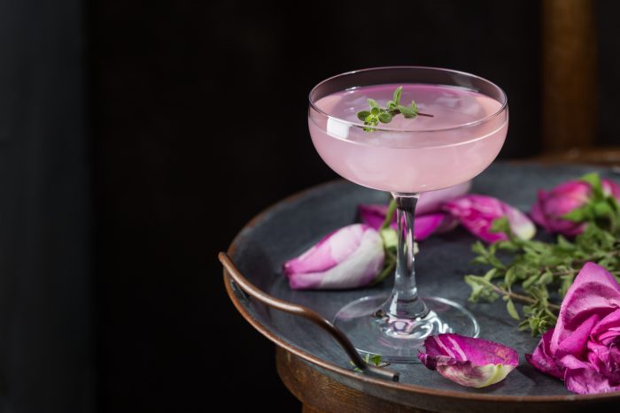 Summer refreshment drinks. Light pink rose cocktail, with rose wine on dark background. With rose flowers. Copy space
